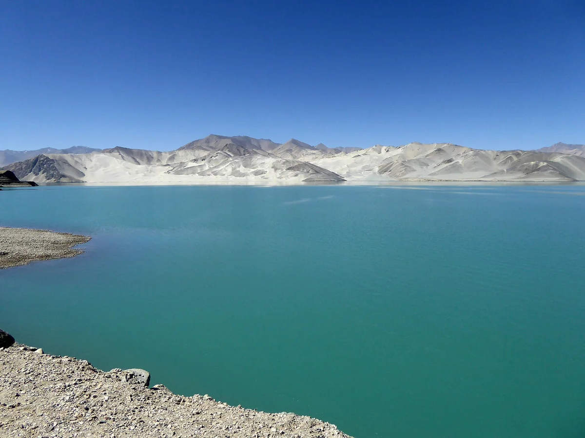 Pale sand mountains meet turquoise water at Pamir’s White Sand Lake.
