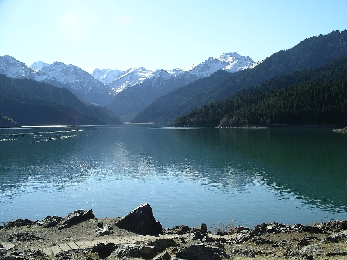 Clear water, spruce forest and distant snowy ridges at Heavenly Lake.