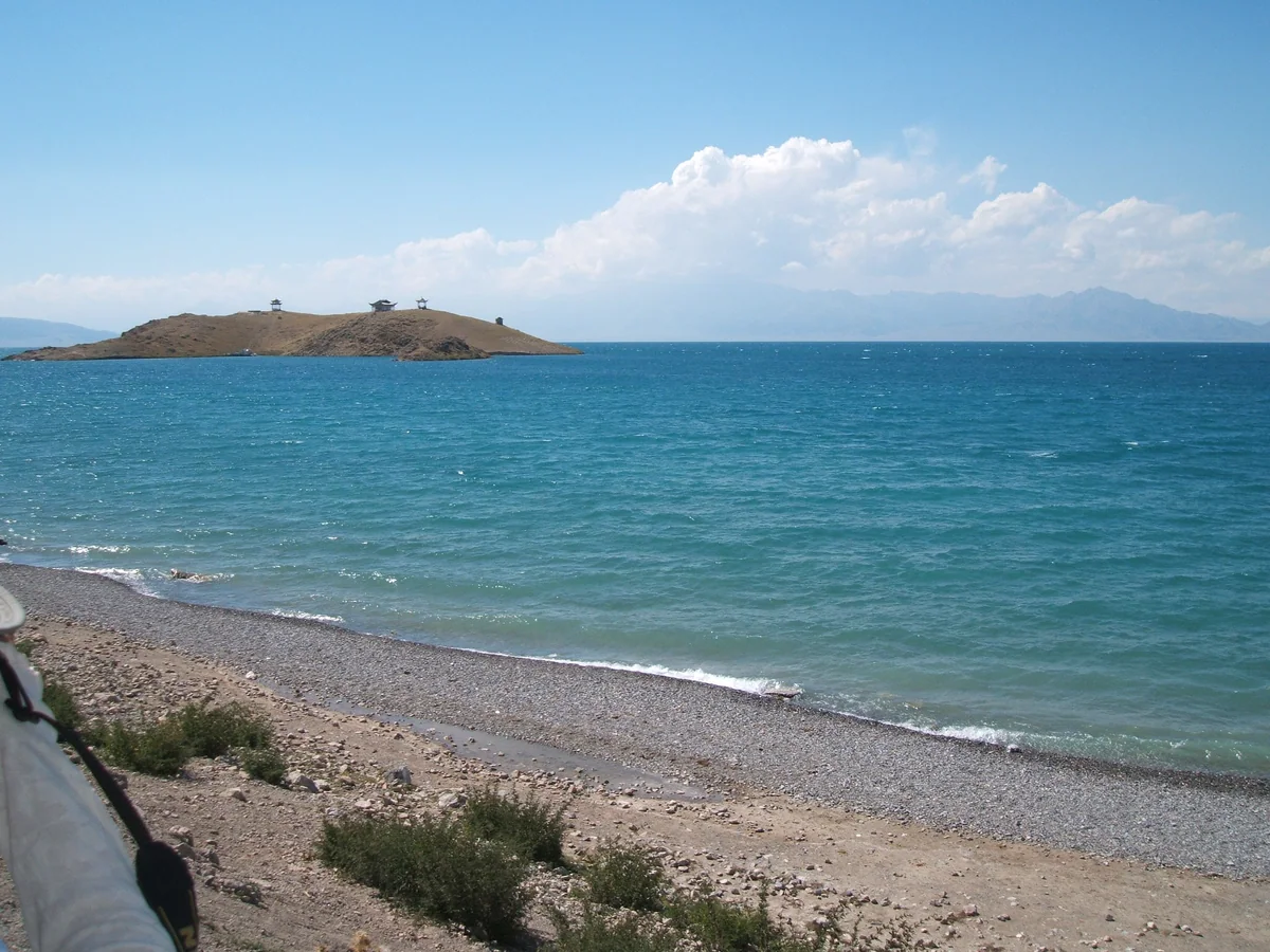An island and shoreline frame the clear blue of Sayram Lake.